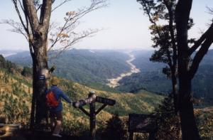帽子を被りリュックを背負った観光客が雁股峠から山の景色を眺めている写真