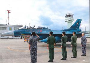 5人の自衛隊員が戦闘機の横に並びそのうち1人が戦闘機に向かい敬礼をしている写真
