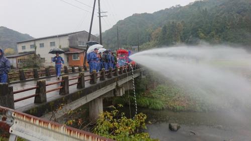 傘をさした消防団員の方々が橋の上から放水訓練をしている写真